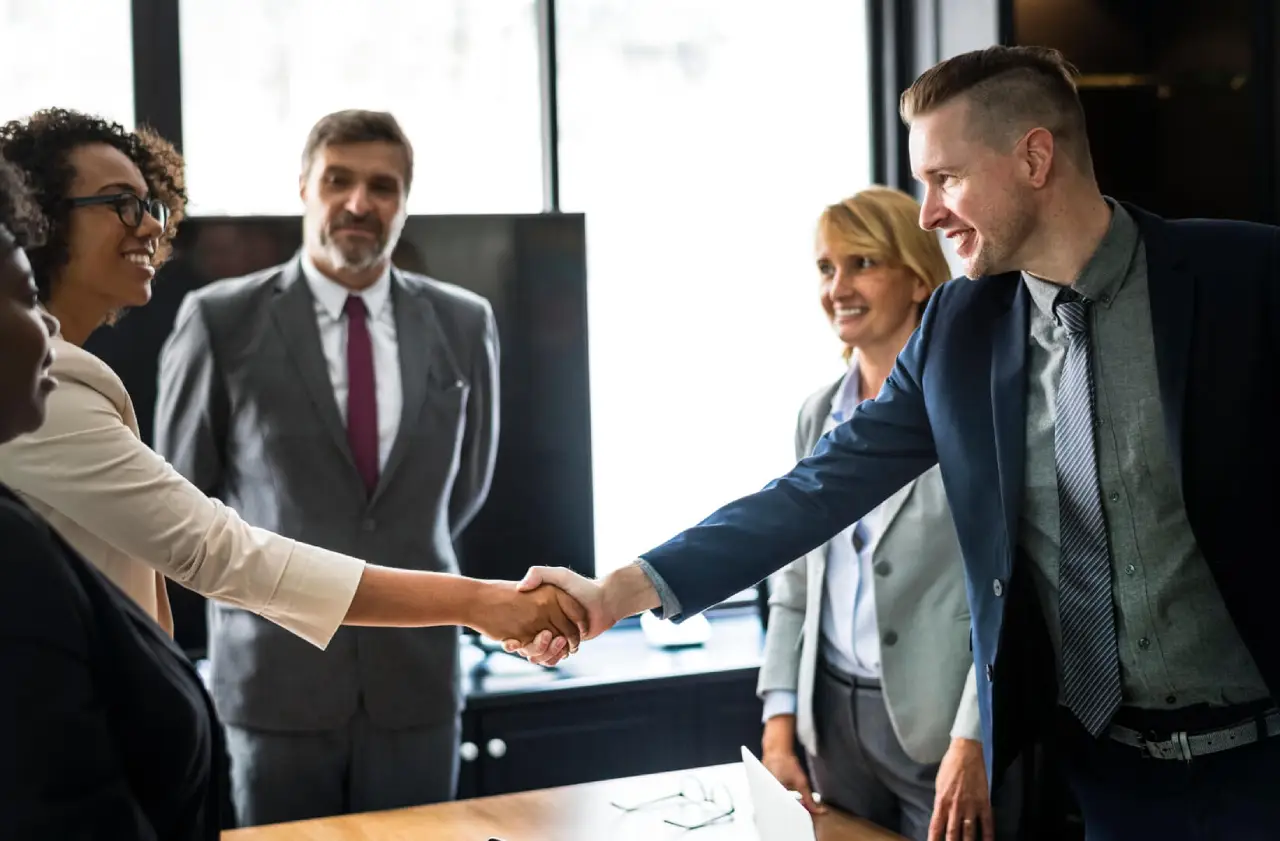 Business professionals shaking hands in an office setting, with colleagues
